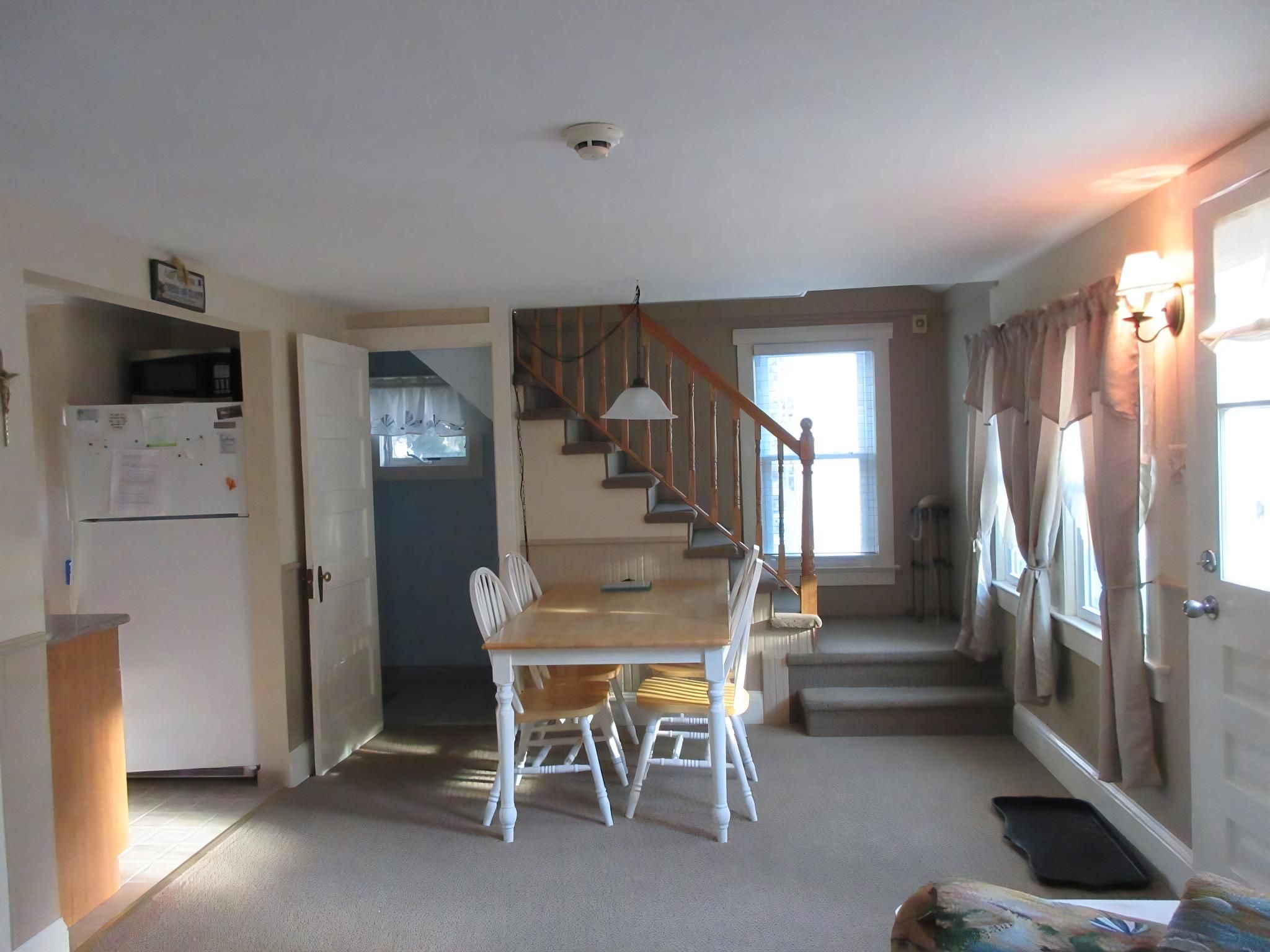 A dining area with a table and chairs, a staircase, a kitchen area, and a door with curtains.