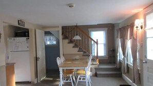 A dining area with a table and chairs, a staircase, a kitchen area, and a door with curtains. - Nice clean rear cottage just 3 homes to the beach in Ship Bottom (Ship Bottom)