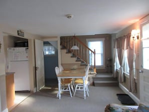 A dining area with a table and chairs, a staircase, a kitchen area, and a door with curtains.