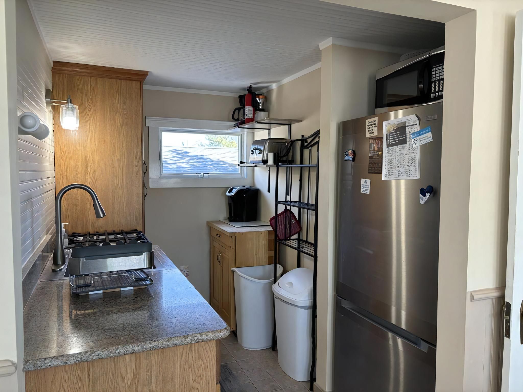 A compact kitchen with a gas stove, a refrigerator, a microwave, and a window providing natural light.