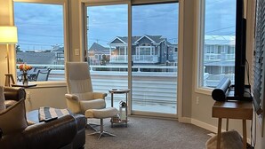 A living room with a ceiling fan, a sofa, a chair, a TV, and large windows with a view of houses. - 4 bedroom accommodation in Harvey Cedars (Harvey Cedars)