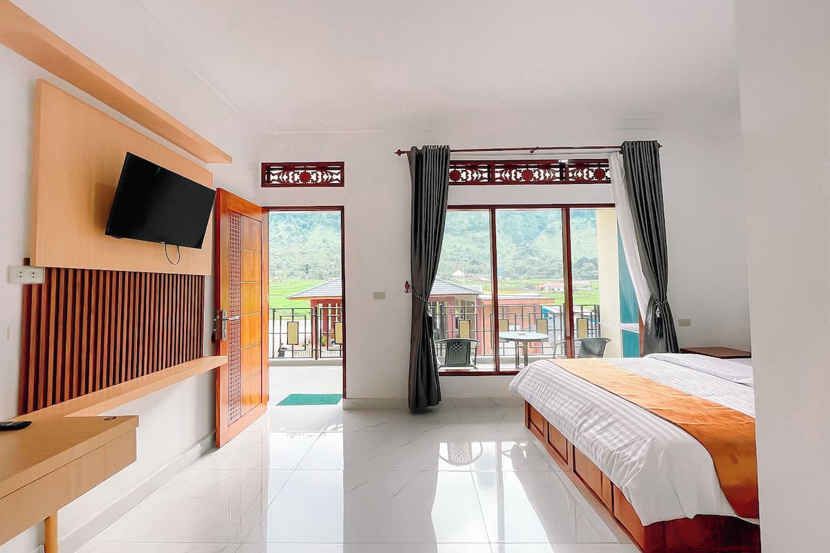 Quarto de hotel com cama, televisão fixada na parede, porta de correr para uma varanda e vista para o exterior.