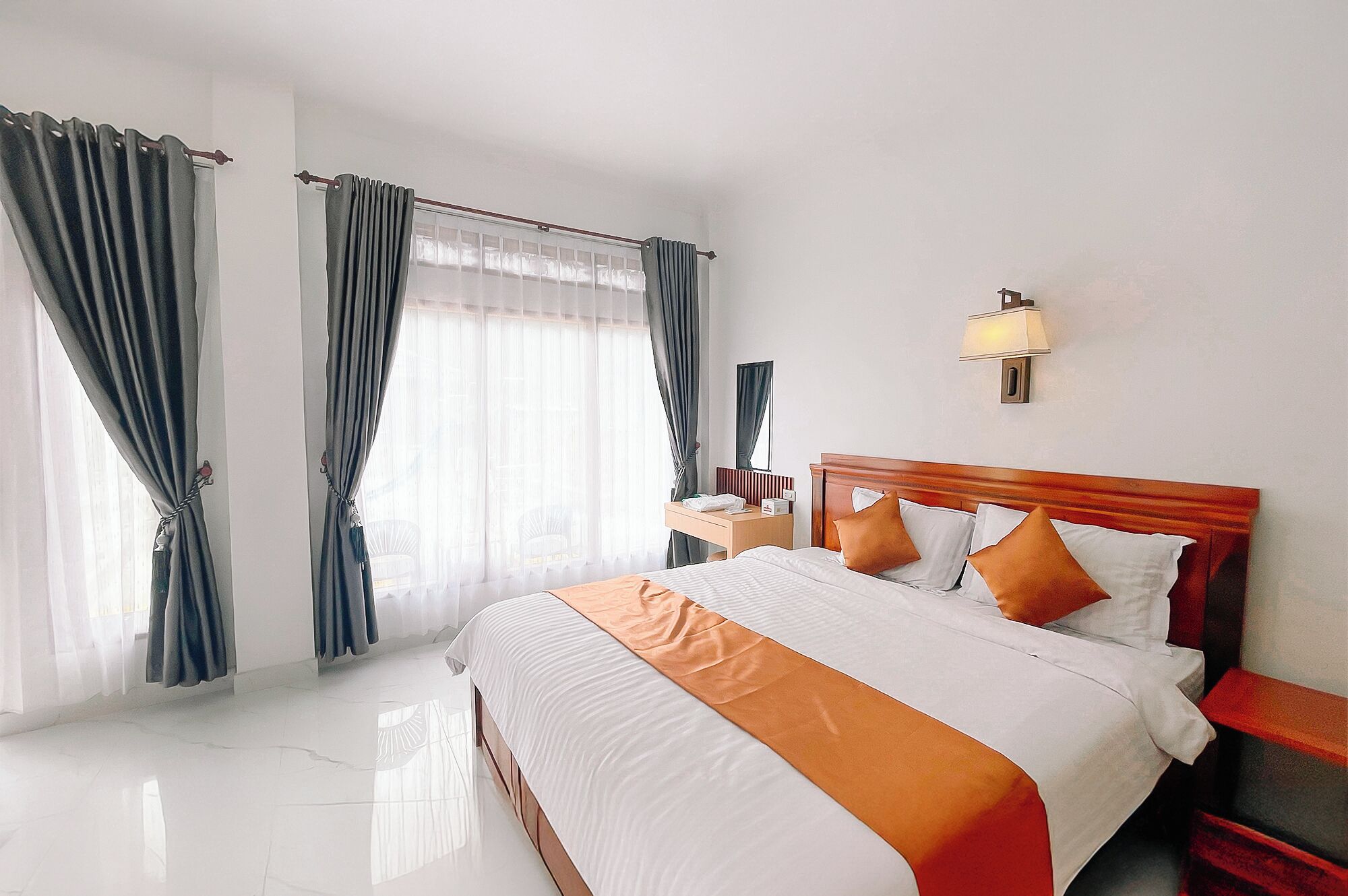 A hotel room with a large bed, a bedside table, a nightstand, a lamp, and a window with curtains.
