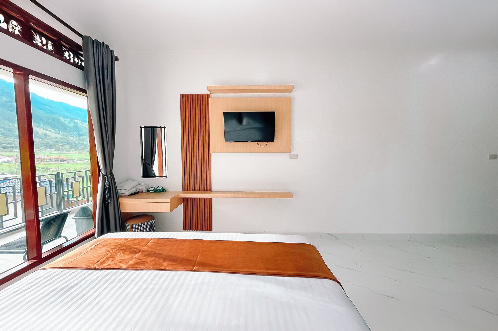 Habitación de hotel con cama, televisor montado en la pared, un escritorio pequeño con silla y ventana con vistas al exterior.