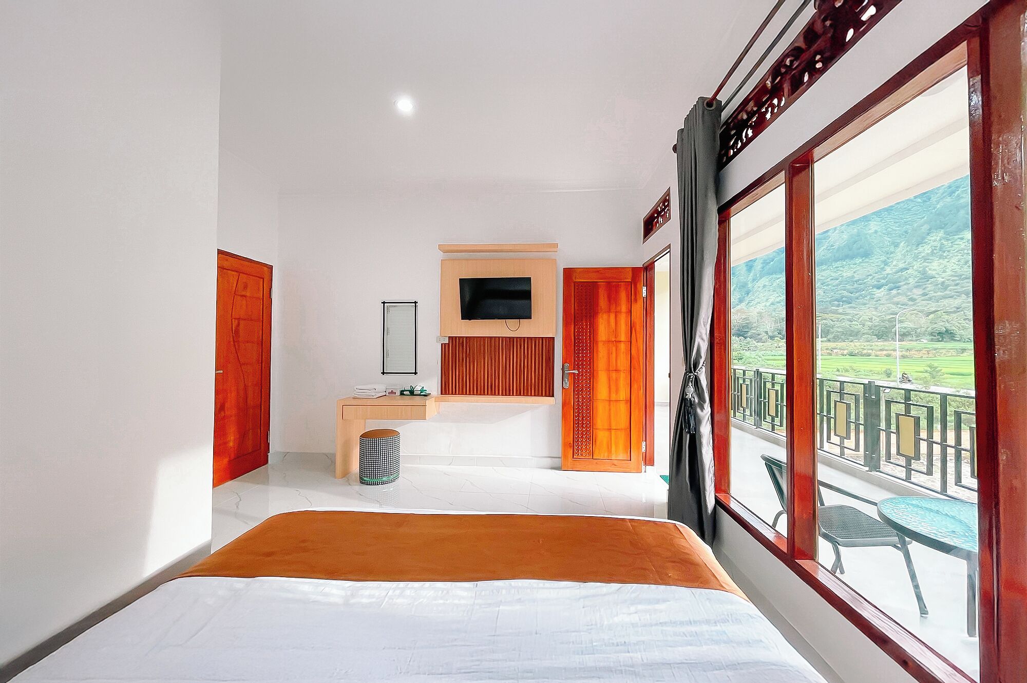 Ein Hotelzimmer mit einem Bett, einem Schreibtisch mit Fernseher, einem Fenster mit Blick auf eine grüne Landschaft und einem Balkon mit Gartenmöbeln.
