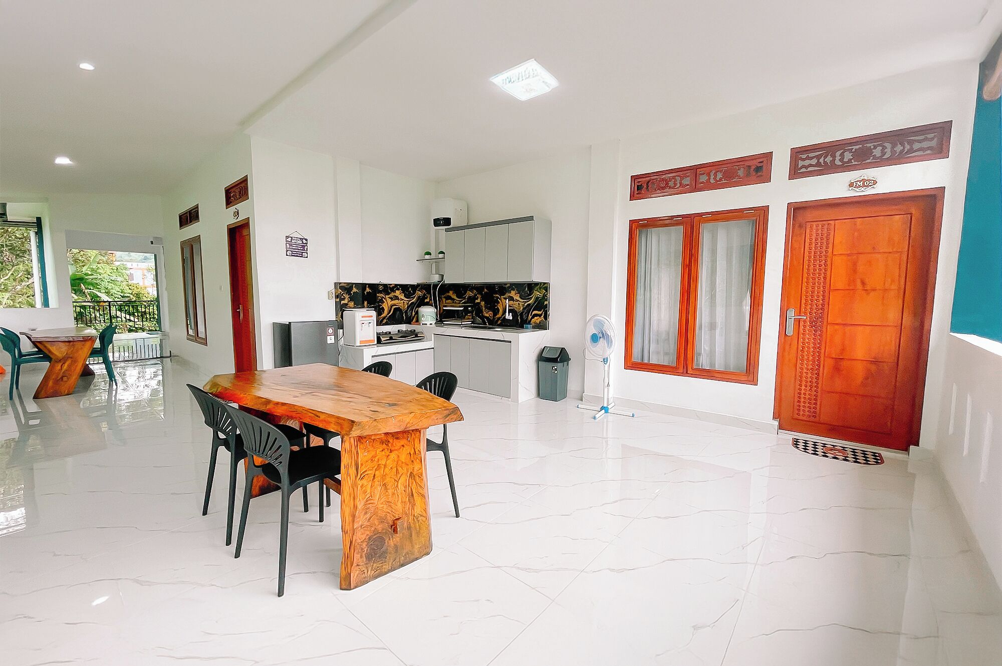 A spacious dining area with a wooden table and chairs, a kitchen with a black and gold backsplash, and a view of greenery outside.