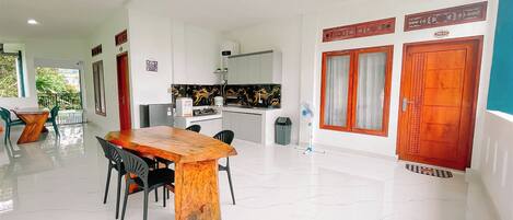 A spacious dining area with a wooden table and chairs, a kitchen with a black and gold backsplash, and a view of greenery outside.
