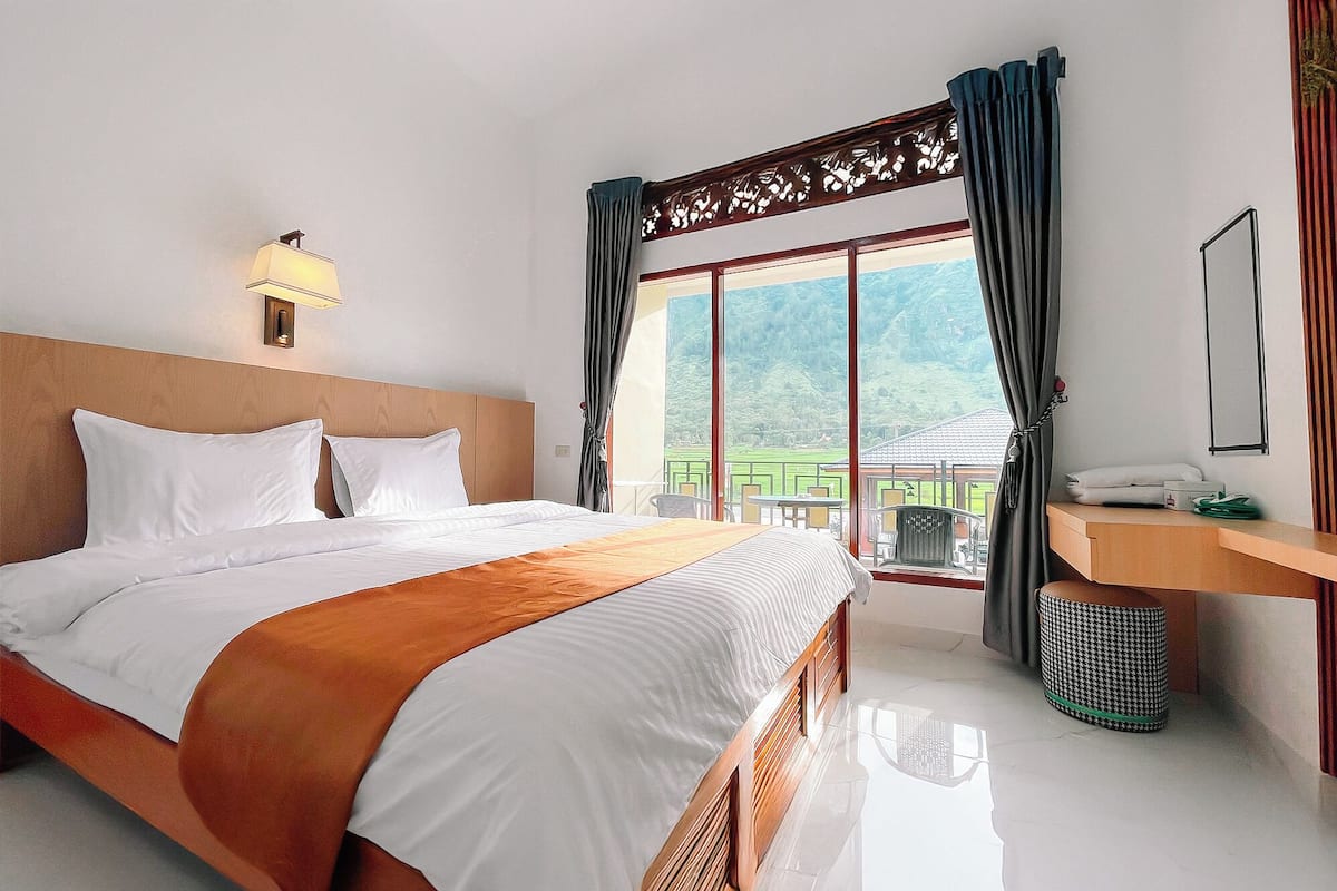 Quarto de hotel com uma cama grande, mesa de cabeceira, espelho e janela com cortinas.