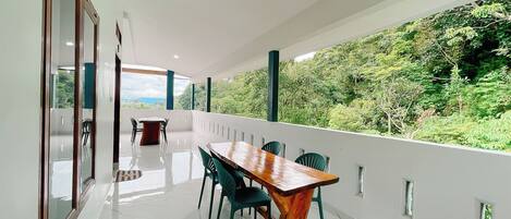 Un espace de restauration moderne avec une table et des chaises en bois, une cloison en verre et une vue sur une végétation luxuriante.