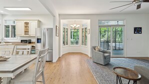 A modern kitchen with white cabinetry, a dining area with a wooden table and chairs, a gray sofa, and a ceiling fan. - 30-Day Rental - Live in Beachside Luxury! 45 Lempesis (Folly Beach)