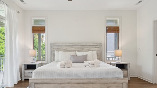 A bedroom with a wooden bed frame, two bedside tables, and a large window with a view of greenery. - 30-Day Rental - Live in Beachside Luxury! 45 Lempesis (Folly Beach)
