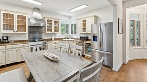 A modern kitchen with white cabinetry, stainless steel appliances, and a wooden dining table. - 30-Day Rental - Live in Beachside Luxury! 45 Lempesis (Folly Beach)