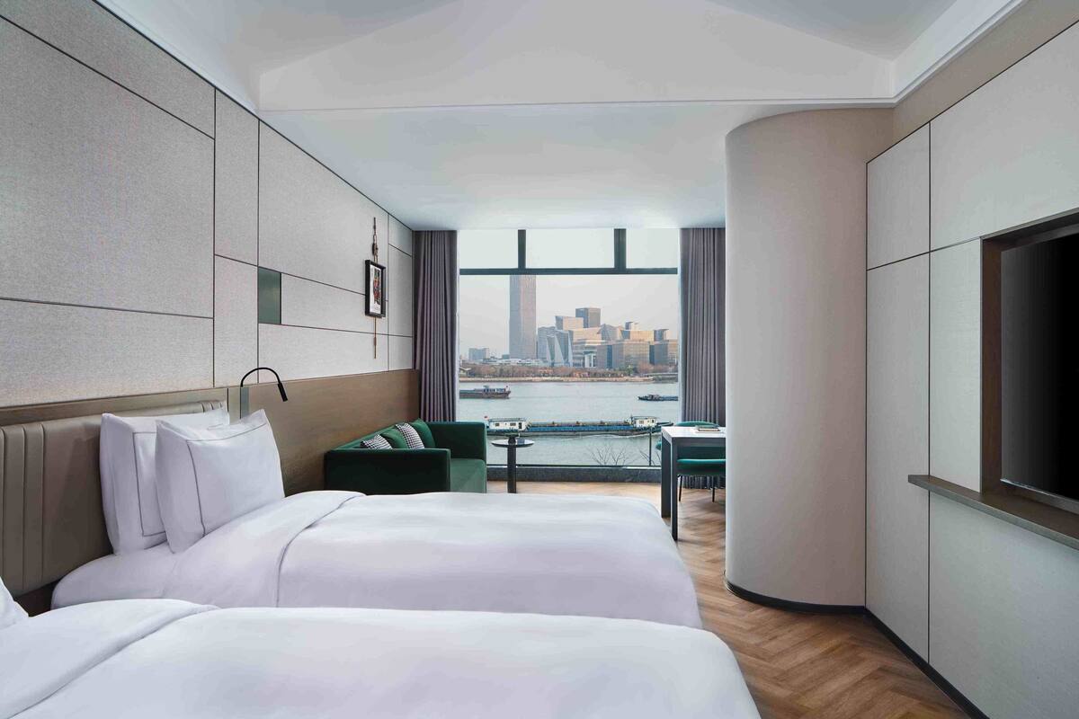 Une chambre d’hôtel avec deux lits, un canapé, une télévision et une vue sur le paysage urbain et la rivière.