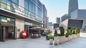 Un hotel moderno con fachada de vidrio, zona de estar al aire libre y una gran estatua de mascota.