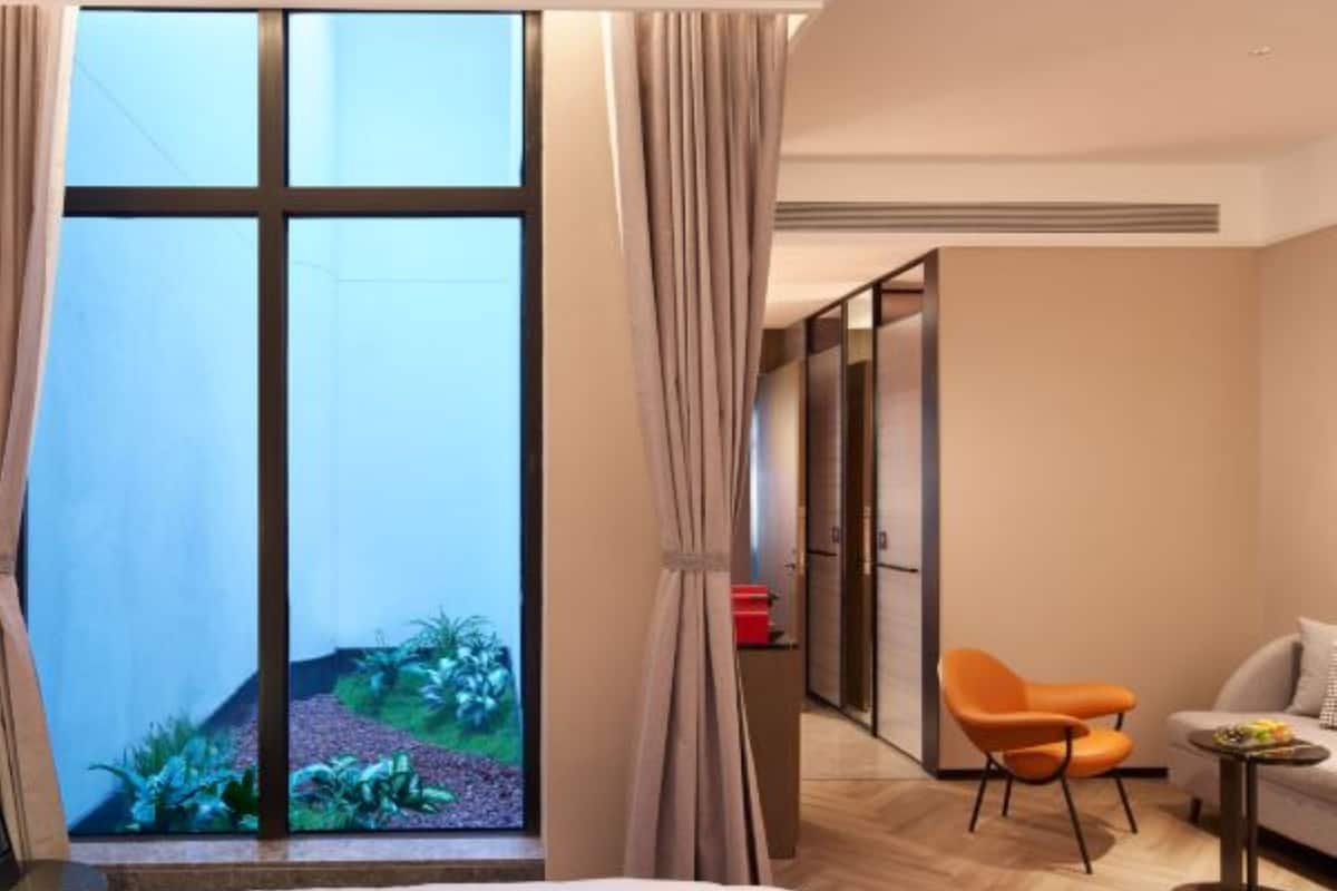 Une chambre d’hôtel avec une grande fenêtre, un lit, un fauteuil orange, une petite table et un canapé.