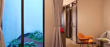 A hotel room with a large window, a bed, an orange chair, a small table, and a sofa.
