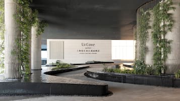 A modern hotel entrance with a large sign, water features, and greenery.
