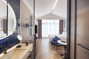 A modern hotel room with a large mirror, a round table, a sofa, and a bed.