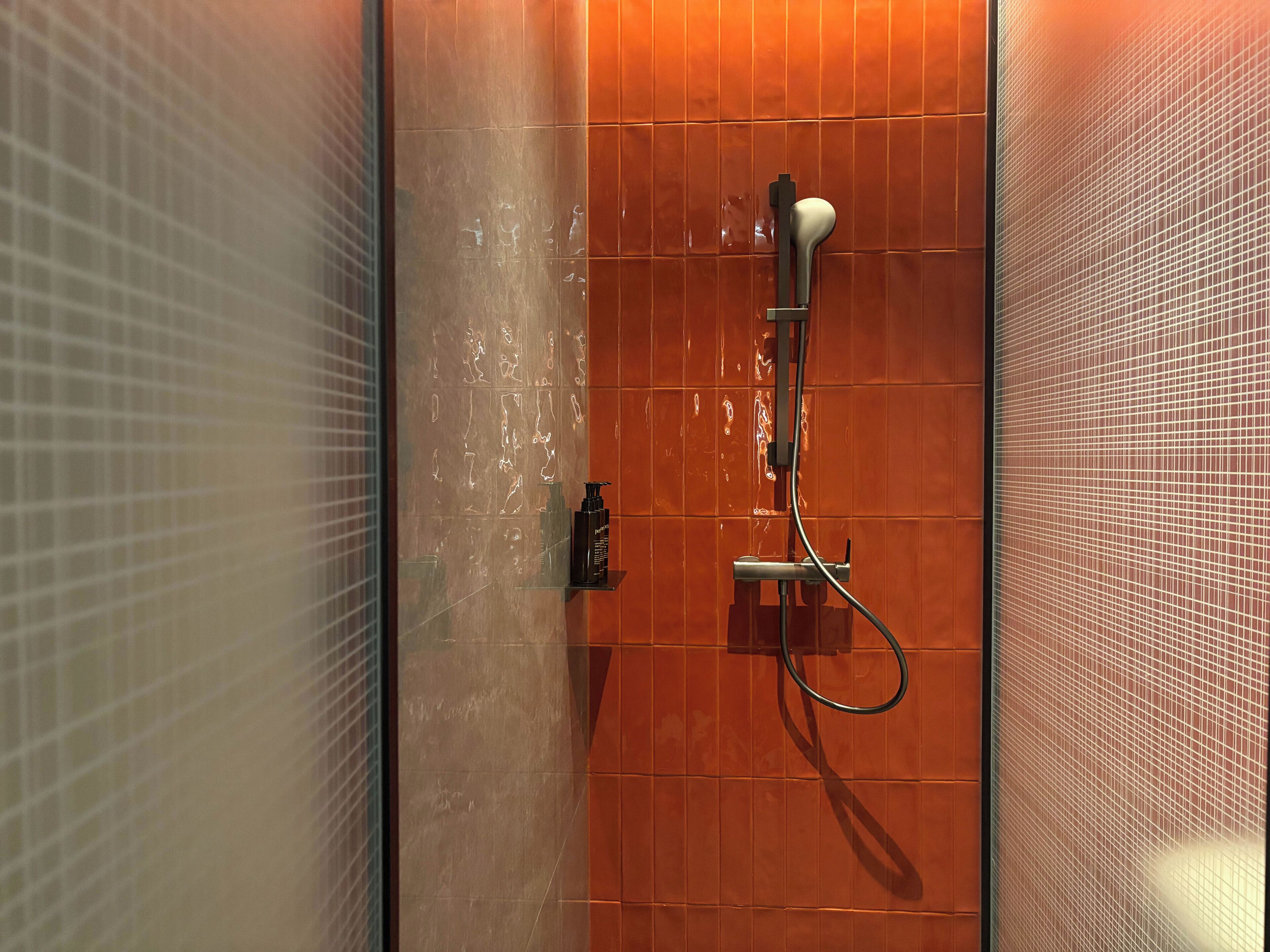 Ducha con cabezal de ducha de mano, panel de control en la pared y puerta de cristal.