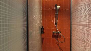 Ducha con cabezal de ducha de mano, panel de control en la pared y puerta de cristal.