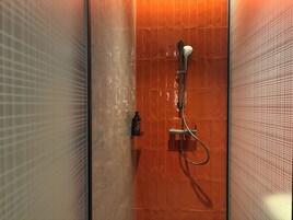 A shower with a handheld showerhead, a wall-mounted control panel, and a glass door.