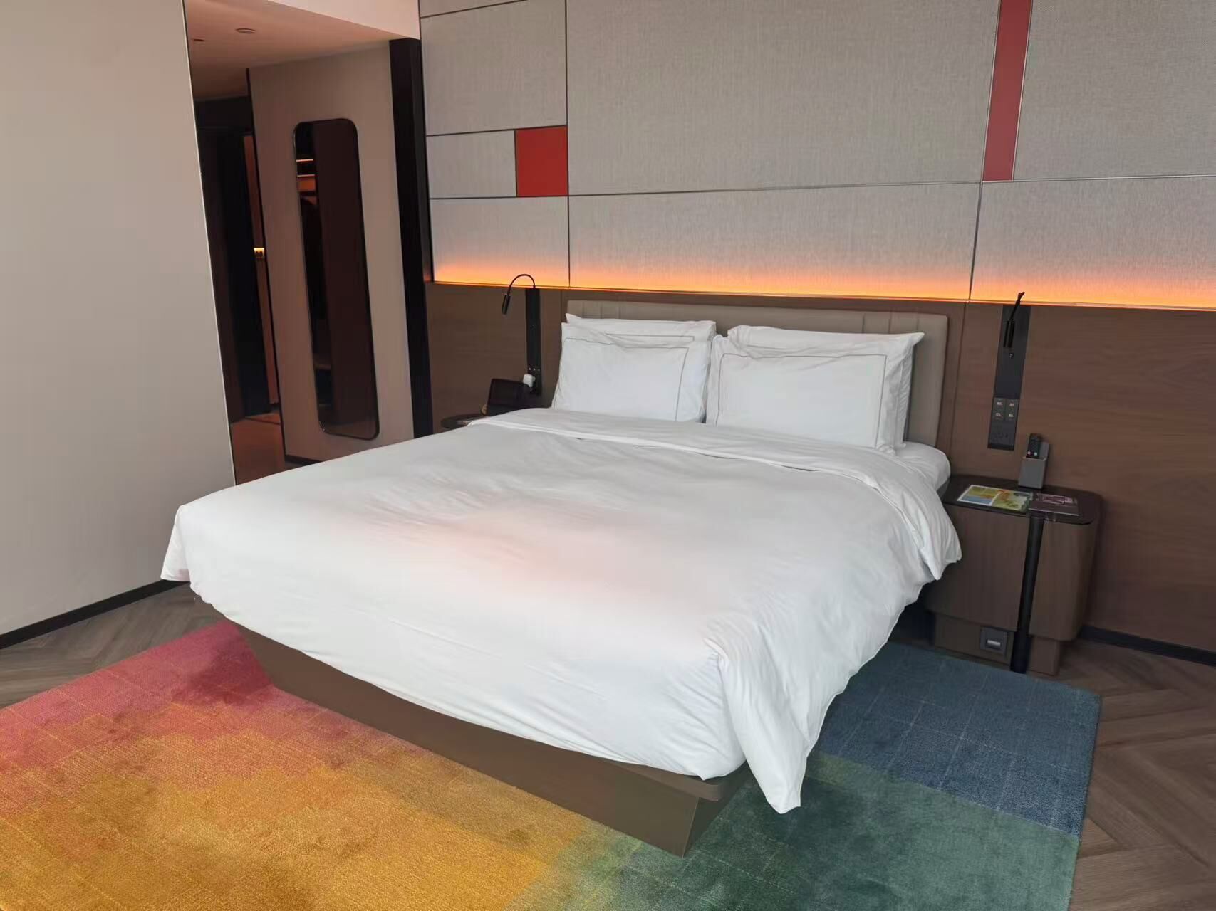 A hotel room with a large bed, a nightstand, a mirror, and a wall with geometric patterns.