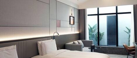 Una habitación de hotel moderna con dos camas, una zona de estar y un amplio ventanal con vistas al verdor.
