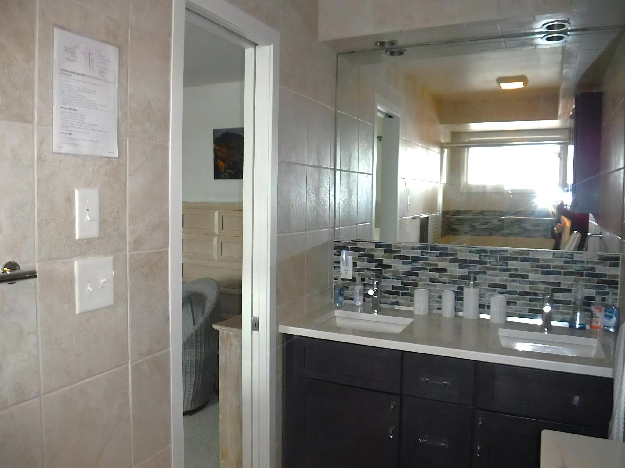 Ein Badezimmer mit gefliesten Wänden, einem Spiegel, einem Waschbecken und einem Schrank.