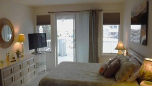 A bedroom with a bed, a TV, a dresser, a lamp, and a window with curtains.