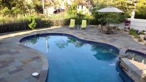 A swimming pool with a curved edge, surrounded by stone tiles and a patio area with chairs and an umbrella. - 170F Sea Pine Dr, LLC 736 (Loveladies)