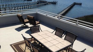 A covered outdoor seating area with a table and chairs, overlooking a body of water with docks. - 170F Sea Pine Dr, LLC 736 (Loveladies)