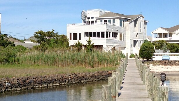 A waterfront property with a wooden dock leading to a house with multiple levels and a balcony. - 170F Sea Pine Dr, LLC 736 (Loveladies)