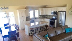 A modern kitchen with white cabinets, a central island with stools, stainless steel appliances, and a dining area with a table and chairs. - 170F Sea Pine Dr, LLC 736 (Loveladies)