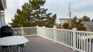 Eine Holzterrasse mit weißer Reling, einem Tisch und einem Grill.