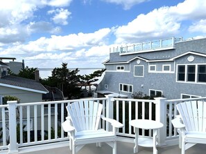 A balcony with white Adirondack chairs and a small round table, overlooking a residential area with a grey house and a view of the water. - 4 bedroom accommodation in North Beach (North Beach)