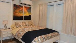Une chambre à coucher comprenant un lit, une table de chevet, un appareil de climatisation et une fenêtre avec des rideaux.