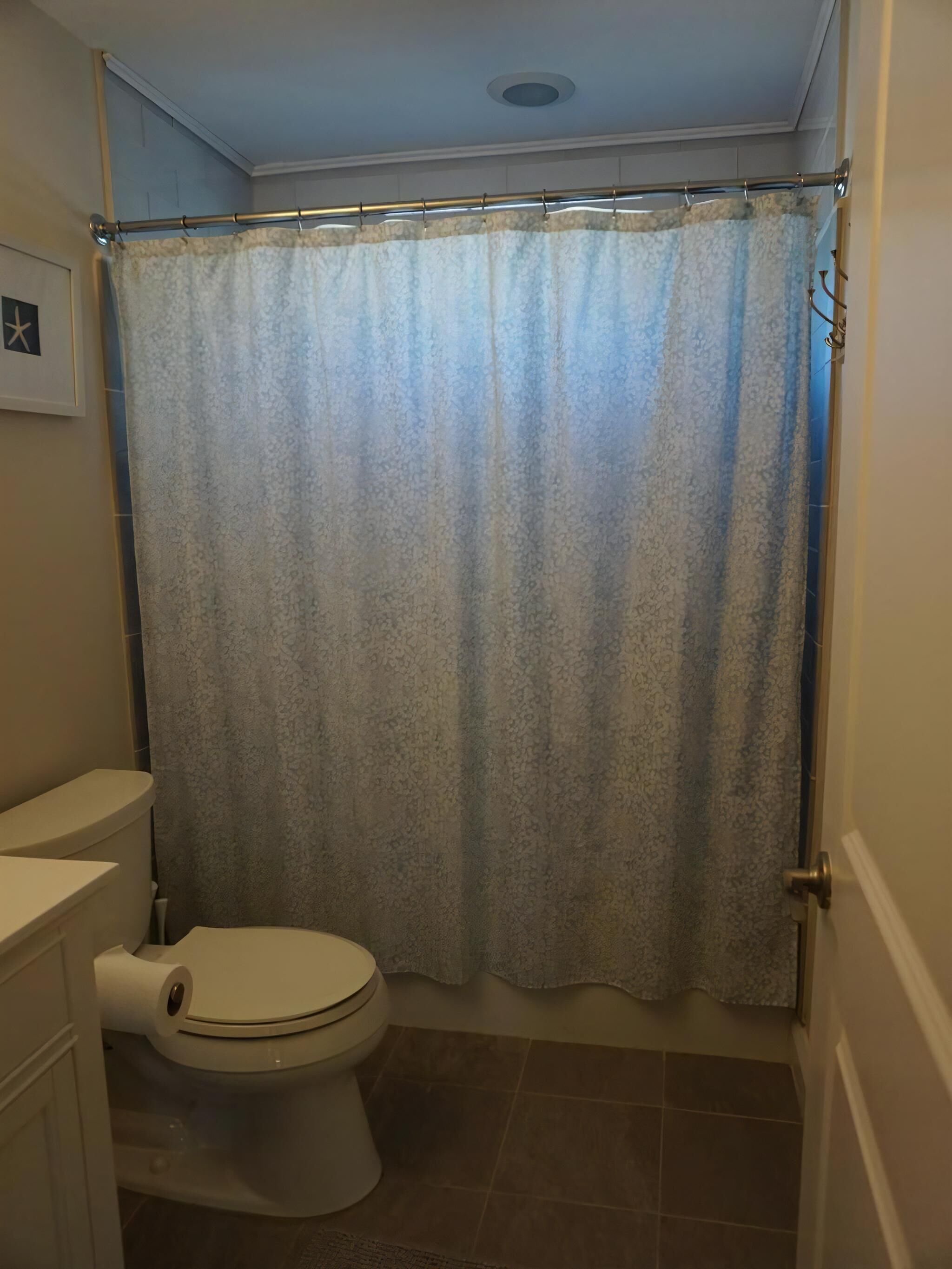 A bathroom with a toilet, shower curtain, and tiled floor.