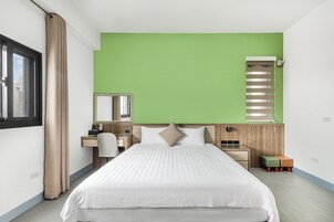 Una habitación de hotel moderna con una cama grande, un escritorio, una silla, un taburete pequeño y una ventana con cortinas.