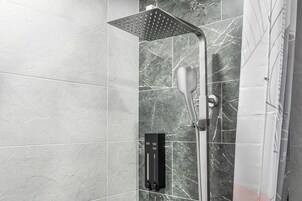 Una ducha moderna con cabezal de ducha tipo lluvia y cabezal de ducha manual, frente a una pared de mármol con panel de control.