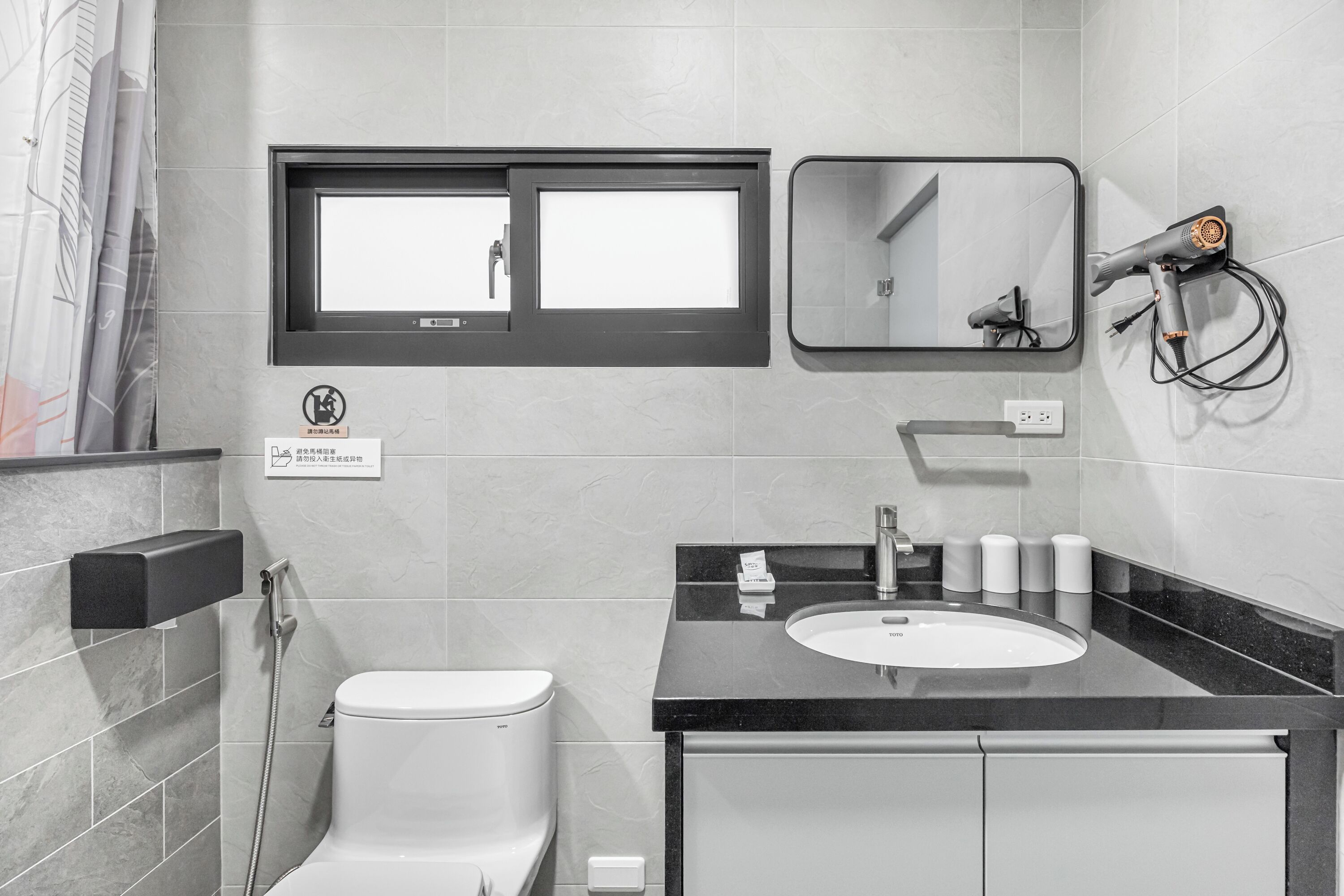 A modern bathroom with a toilet, sink, and a hairdryer mounted on the wall.