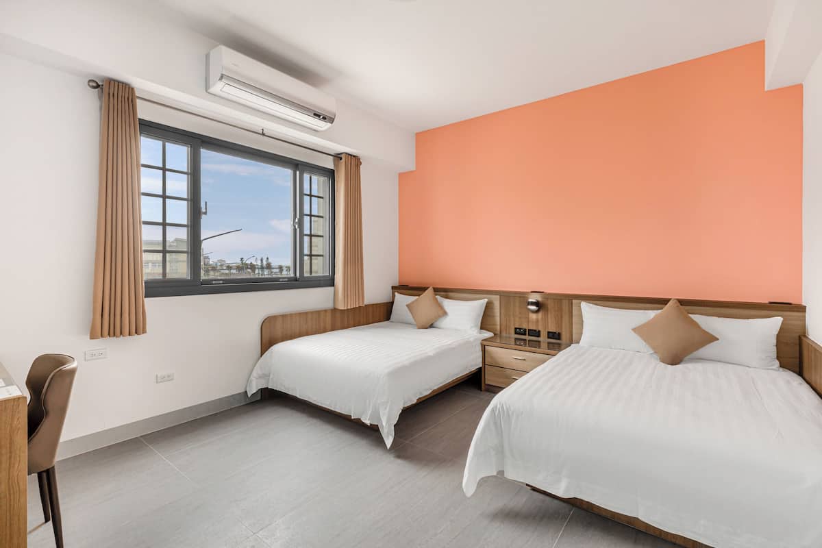 A hotel room with two beds, a desk, and a window with curtains.