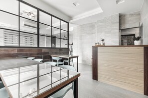 A modern kitchen with a glass-top dining table, light-colored tiles, and a wooden accent wall. - Siricoast House (Magong)