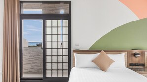 Habitación de hotel con cama, cabecera de madera, vista a través de una puerta corrediza de vidrio y una pared de acento verde.