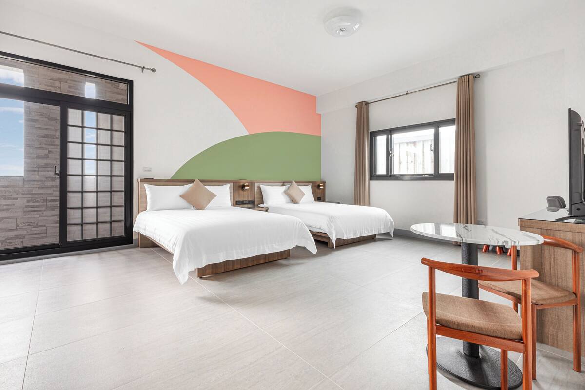 A hotel room with two beds, a dining table, and a large window.