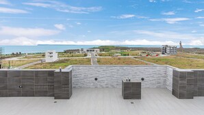 Una terraza en la azotea con vistas a la costa, incluyendo edificios y una estatua.