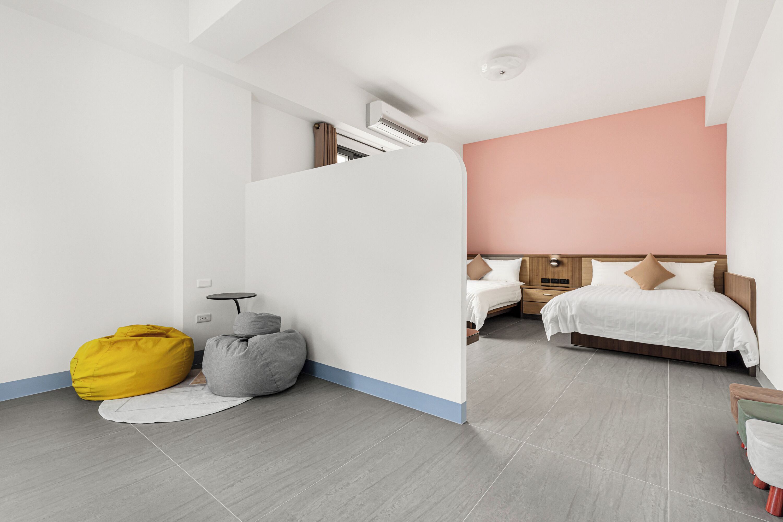 A modern hotel room with a bed, bedside tables, a sofa, and a small seating area with bean bags.