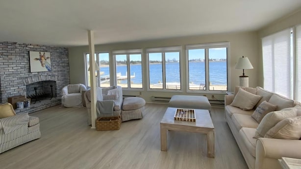 Ein Wohnzimmer mit Kamin, einer Couch, einem Couchtisch und großen Fenstern mit Meerblick.