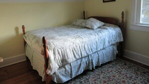 Un lit simple dans une chambre avec une tête de lit en bois, un tapis à motifs floraux et un tableau encadré au mur.