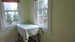 Une pièce d ’angle avec deux fenêtres, une table recouverte d’une nappe et un tapis à motifs sur le sol.