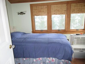 A bedroom with a bed, a window with blinds, and an air conditioning unit.